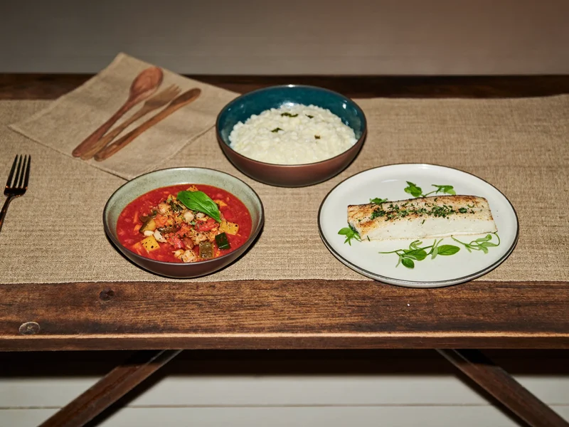 Minestrone, risotto e pesce al forno in ciotole di ceramica rustica
